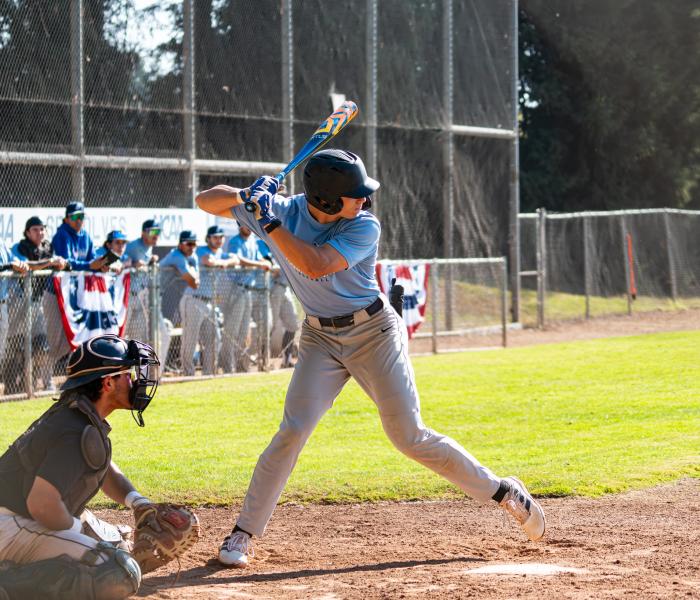 Student with bat in hand and team behind them in dugout