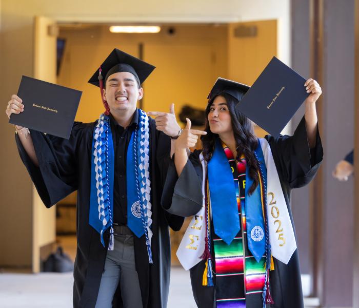 2 graduate student pointing at their diploma