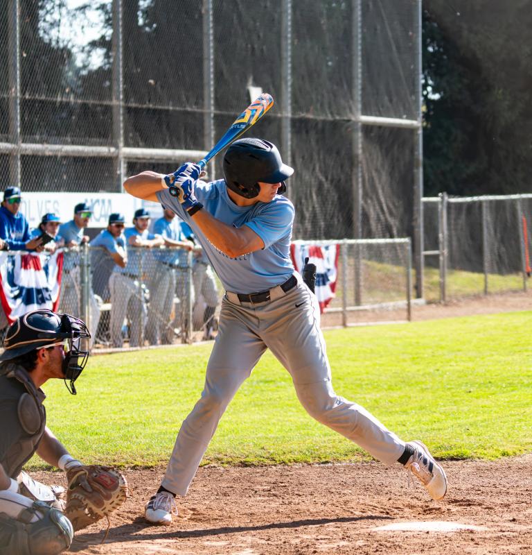 Student with bat in hand and team behind them in dugout