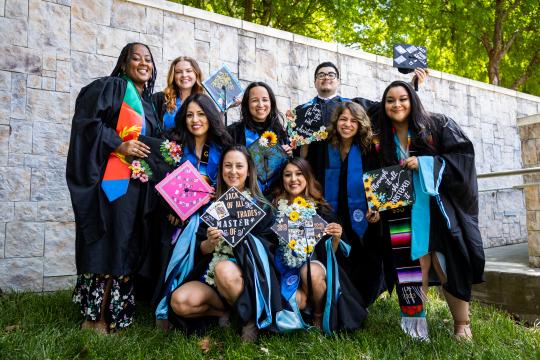 Students in grad regalia in a group photo holding their caps