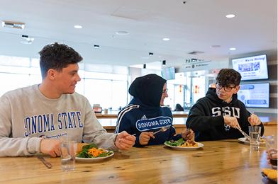 Three students with plates of food infront of them in the dining hall on campus