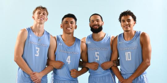 Four basketball players standing smiling towards a camera