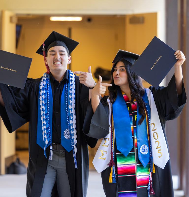 2 graduate student pointing at their diploma