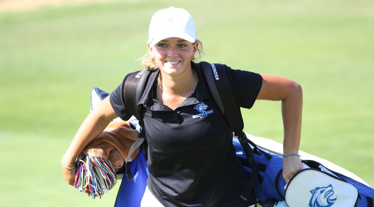 An SSU student carrying golf clubs while playing on the Women's Golf team