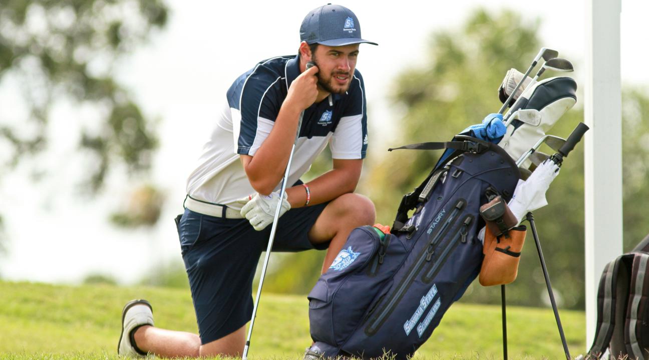 An SSU student crouching on the green while playing on the Men's Golf team