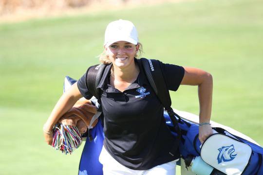 An SSU student carrying golf clubs while playing on the Women's Golf team