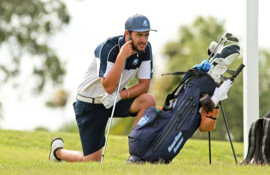 An SSU student crouching on the green while playing on the Men's Golf team